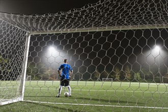USA, California, Ladera Ranch, goalie on illuminated soccer field at night.