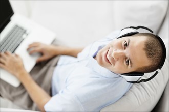 South Africa, Young man wearing headphones sitting on sofa and using laptop, high angle view. Photo
