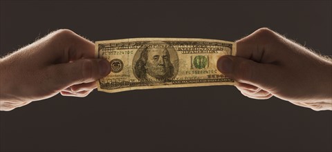 Hands holding one hundred dollar bill. Photo : Mike Kemp