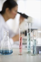 USA, New Jersey, Jersey City, Female scientist using microscope behind test tubes and flasks.