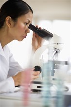 USA, New Jersey, Jersey City, Female scientist using microscope behind test tubes.