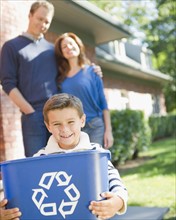 USA, New York, Flanders, Boy (8-9) holding bucket with recycling symbol, parents in background.
