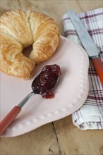 Croissant with jam on plate.
