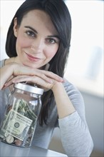 Portrait of young smiling woman with savings in jar.