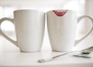 Close up of coffee mugs, one with red lipstick sign on edge. Photo : Jamie Grill Photography