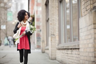 USA, Washington State, Seattle, Young woman walking in street carrying bunch of tulips. Photo :
