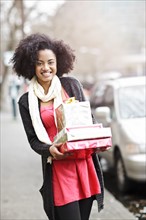 USA, Washington State, Seattle, Young cheerful woman carrying stack of boxed gifts. Photo : Take A