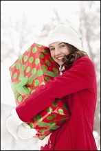 USA, Utah, Lehi, Portrait of young woman hugging Christmas gift outdoors. Photo : Mike Kemp