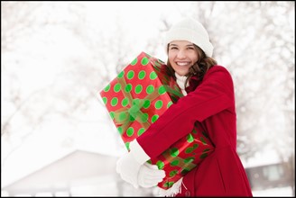 USA, Utah, Lehi, Portrait of young woman hugging Christmas gift outdoors. Photo : Mike Kemp