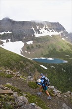 USA, Montana, Glacier National Park, Mid adult woman hiking with backpack during rain. Photo : Noah