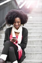 USA, Washington State, Seattle, young woman sitting on steps and text messaging. Photo : Take A Pix