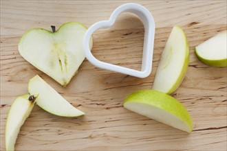 Heart shaped apples with cutter on chopping board.