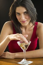 Portrait of young woman drinking martini, studio shot.