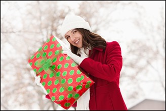 USA, Utah, Lehi, Portrait of young woman holding Christmas gift outdoors. Photo : Mike Kemp