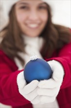 Portrait of young woman holding Christmas bauble outdoors. Photo : Mike Kemp