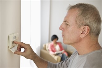 Mature man adjusting room temperature, while woman is sitting in background.