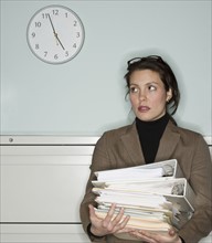 Young woman in office holding stack of documents.