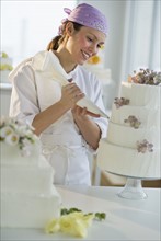 Happy young woman decorating wedding cake.