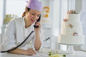 Happy young woman taking order near wedding cake.