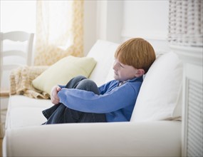 Boy (8-9) sitting on sofa. Photo : Jamie Grill Photography