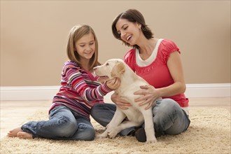 Mother and daughter (10-11) playing with Labrador on carpet. Photo : Mike Kemp