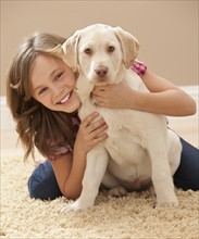 Portrait of girl (10-11) embracing Labrador on carpet. Photo : Mike Kemp