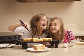 Two girls (10-11) preparing toast in kitchen. Photo : Mike Kemp