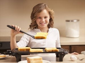 Portrait of girl (10-11) preparing toast in kitchen. Photo : Mike Kemp