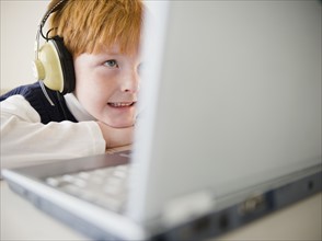 Boy (8-9) wearing headphones, using laptop. Photo : Jamie Grill Photography