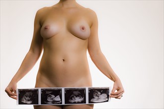 Studio shot of naked pregnant woman holding ultrasonography picture. Photo : Noah Clayton