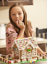 Portrait of girl (6-7) licking finger by gingerbread house. Photo : Mike Kemp