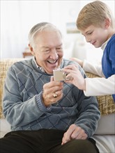 Grandfather and grandson (8-9) holding digital camera. Photo : Jamie Grill Photography