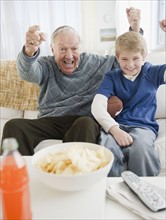Grandfather and grandson (8-9) watching tv and cheering. Photo : Jamie Grill Photography
