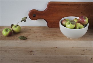 Close up of apples on table with bawl and cutting board.