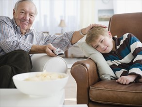 Grandfather stroking grandson (8-9) and watching tv. Photo : Jamie Grill Photography