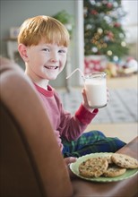 Portrait of boy (8-9) holding milk and cookies on Christmas Eve. Photo : Jamie Grill Photography