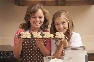 Portrait of two girls (10-11) holding biscuits in kitchen. Photo : Mike Kemp