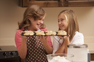 Two girls (10-11) holding biscuits in kitchen. Photo : Mike Kemp