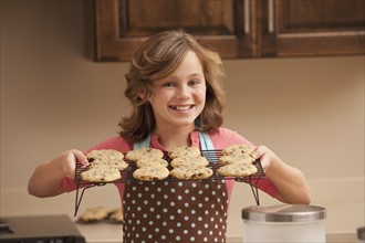 Portrait of girl (10-11) holding biscuits in kitchen. Photo : Mike Kemp