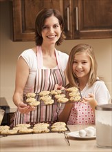 Portrait of mother holding biscuits with daughter (10-11) in kitchen. Photo : Mike Kemp
