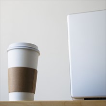 Coffee cup beside laptop in office. Photo : Joe Clark
