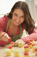 Portrait of young woman decorating cupcakes in kitchen. Photo : Mike Kemp