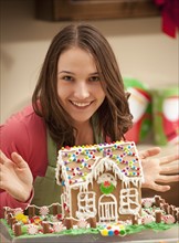 Portrait of young woman with gingerbread house in kitchen. Photo : Mike Kemp