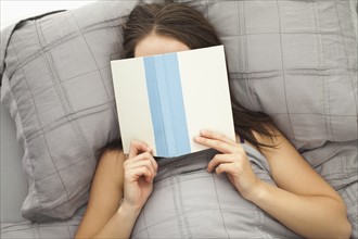 Young woman reading in bed. Photo : Mike Kemp