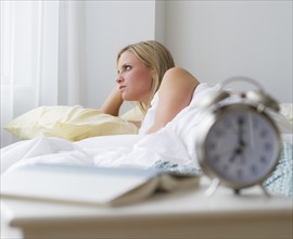 Woman in bed with alarm clock in foreground. Photo : Daniel Grill