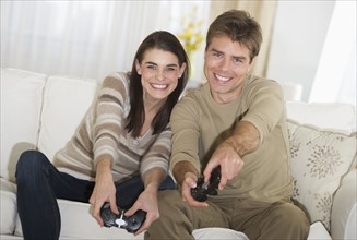 Couple sitting on sofa, playing video games.