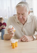 Grandfather holding pill bottle, grandson (8-9) in background. Photo : Jamie Grill Photography