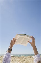 USA, Massachusetts, woman's hands on beach holding book. Photo : Chris Hackett