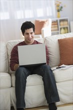 Man using laptop on sofa.