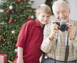 Grandfather and grandson (8-9 years) taking picture, christmas tree in background. Photo : Jamie